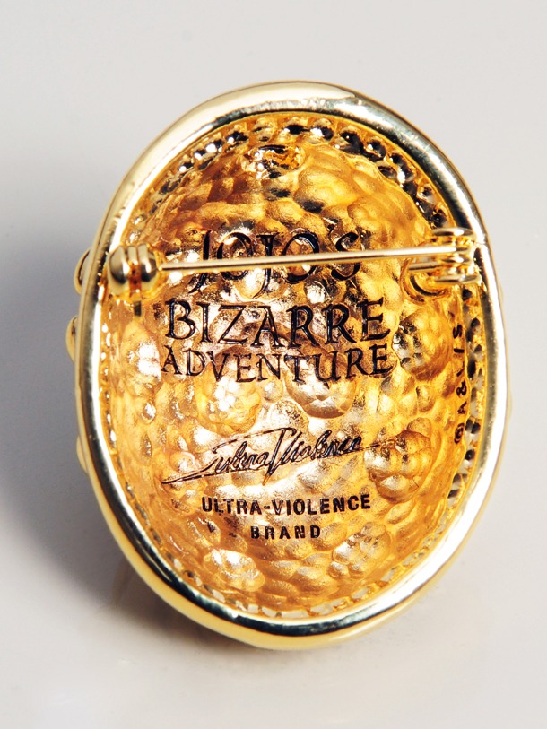 「ジョルノ・ジョバーナ ブローチ」の裏側。JOJO'S BIZARRE ADVENTUREの文字が刻まれている。(C)Hirohiko Araki ＆ LUCKY LAND COMMUNICATIONS / SHUEISHA.
