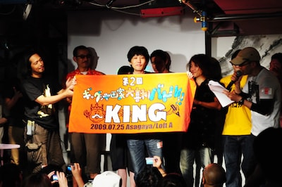 第2回「ギャグ漫画家大喜利バトル」キングの座に輝いたとり・みき。寺田克也より贈呈された勝者の証を掲げる姿は、王者の風格を漂わせている。