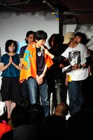 優勝賞品のタオルを羽織り、インタビューを受けるとり。右は月刊コミックビーム副編集長、岩井好典氏。