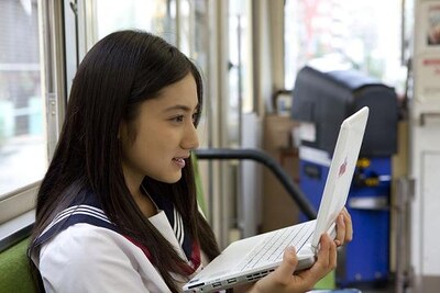 「紗綾が、クラブサンデーを読んでみた。」から、都電の車内で朗読をする1シーン。いつでもどこでも手軽にウェブマンガを読むことができる、テクノロジーの進歩は果てしない。