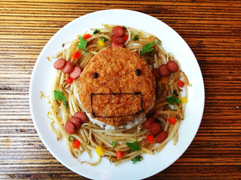 味噌じゃがコロッケに味噌カツソースでオリゼーが描かれたA・オリゼーライス。コロッケの下にはご飯。周りにもやしのキムチ炒めが散らされている。950円。