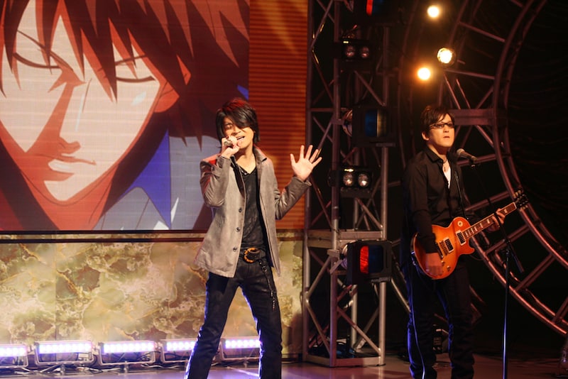アニメ「テニスの王子様」の映像をバックに熱唱する許斐剛（左）とUZA（右）。