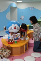 マンガを読むドラえもんと戯れる21世紀の子供たち。(c)Fujiko-Pro