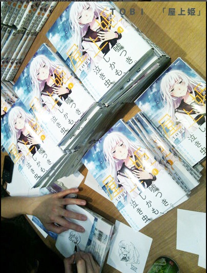 「屋上姫」4巻にTOBIがサインする様子。