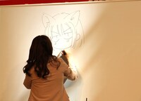 ホワイトボードに自画像を描く種村。