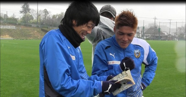 単行本を読み込む中村憲剛と大久保嘉人。(c)Jリーグ×キャプテン翼 DREAMSHOOT製作委員会
