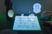 のび太とドラえもんの立体映像で、マンガの製作工程を説明。 (c)Fujiko-Pro