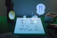 のび太とドラえもんの立体映像で、マンガの製作工程を説明。 (c)Fujiko-Pro