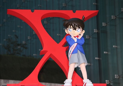 紅に染まった「Xロゴ」の前で、Xポーズを披露する江戸川コナン。