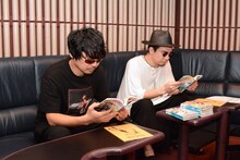 伊豆乃風の寿竜次郎を演じる小西克幸（左）と、時田信治を演じる安元洋貴（右）が、「ぐらんぶる」を真剣に読む様子。