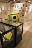 「新隊員イラスト」コーナーの近くには、グッズを展示するガラスケースも。ケロロも自分のグッズには興味津々。