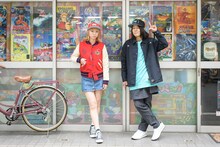 「ゲームセンターあらし」のインベーダーキャップの着用イメージ。元ベイビーレイズJAPANのリコピンこと大矢梨華子とKICK THE CAN CREWのMCUがモデルを務めている。