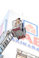 高所から指揮を支援する梶原岳人と、ヤマダ電機の看板。