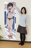 A賞「宝多六花 等身大ビジュアルクロス」を壁に貼ったところ。横に並んだスタッフとの比較で、大きさがわかる。