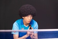 ドラマ「WOWOWオリジナルドラマ アフロ田中」より、卓球のユニフォームを身にまとい、ラケット代わりに携帯を手にする田中。