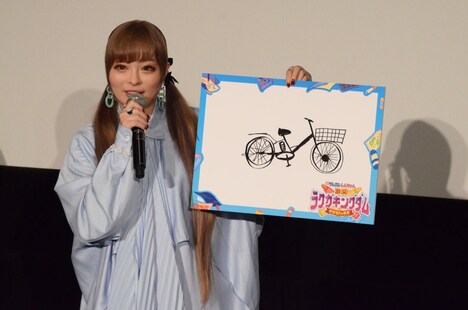 電動自転車が書かれたボードを掲げるきゃりーぱみゅぱみゅ。