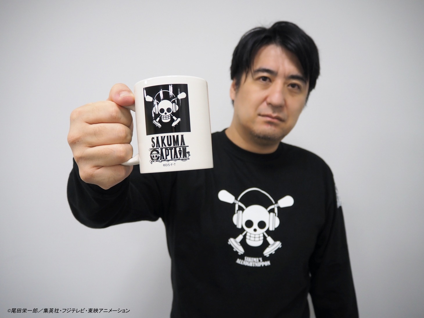 コラボグッズのマグカップを掲げる佐久間宣行。