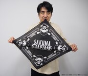 コラボグッズのバンダナを広げる佐久間宣行。