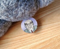 おじさんが描かれた「ねこに転生したおじさん プンちゃん 等身大ぬいぐるみ」のネームタグ。