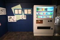 「画業10周年記念 コトヤマ展」の様子。「よふかしのうた」エリアに設置された自動販売機のボタンを押すと……。