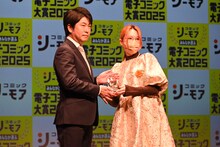 「華麗に離縁してみせますわ！」の漫画を手がけるあばたもがトロフィーを受け取る様子。