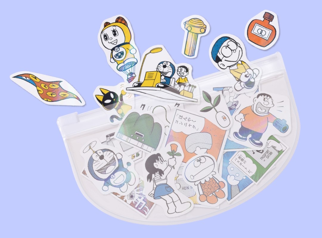 「『とっておきドラえもん　あったらいいなひみつ道具編』特別版」に付属する「スペアポケット型ジップバッグ」と「全50種類以上！ひみつ道具フレークホロシール」。
