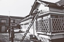 1970年頃、中野坂上に移転したAプロダクション社屋にて看板を描く大塚康生。下で見上げているのはアニメーターの楠部大吉郎（右）と芝山努（撮影：南正時）