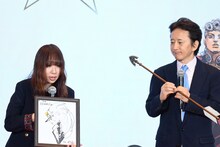 荒木飛呂彦の描き下ろした色紙を持つ、バンダイナムコエクスペリエンスの久家麻衣子氏