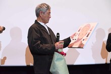 似顔絵を見つめる小林薫