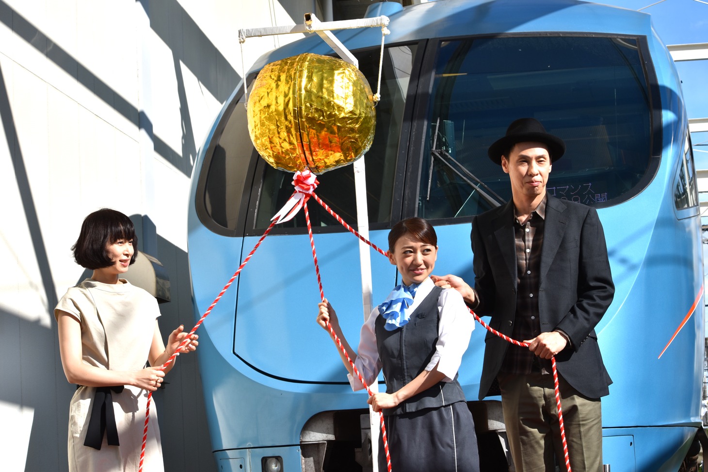ロマンスカーの前でくす玉を割る体勢を取る大島優子、大倉孝二、タナダユキ。