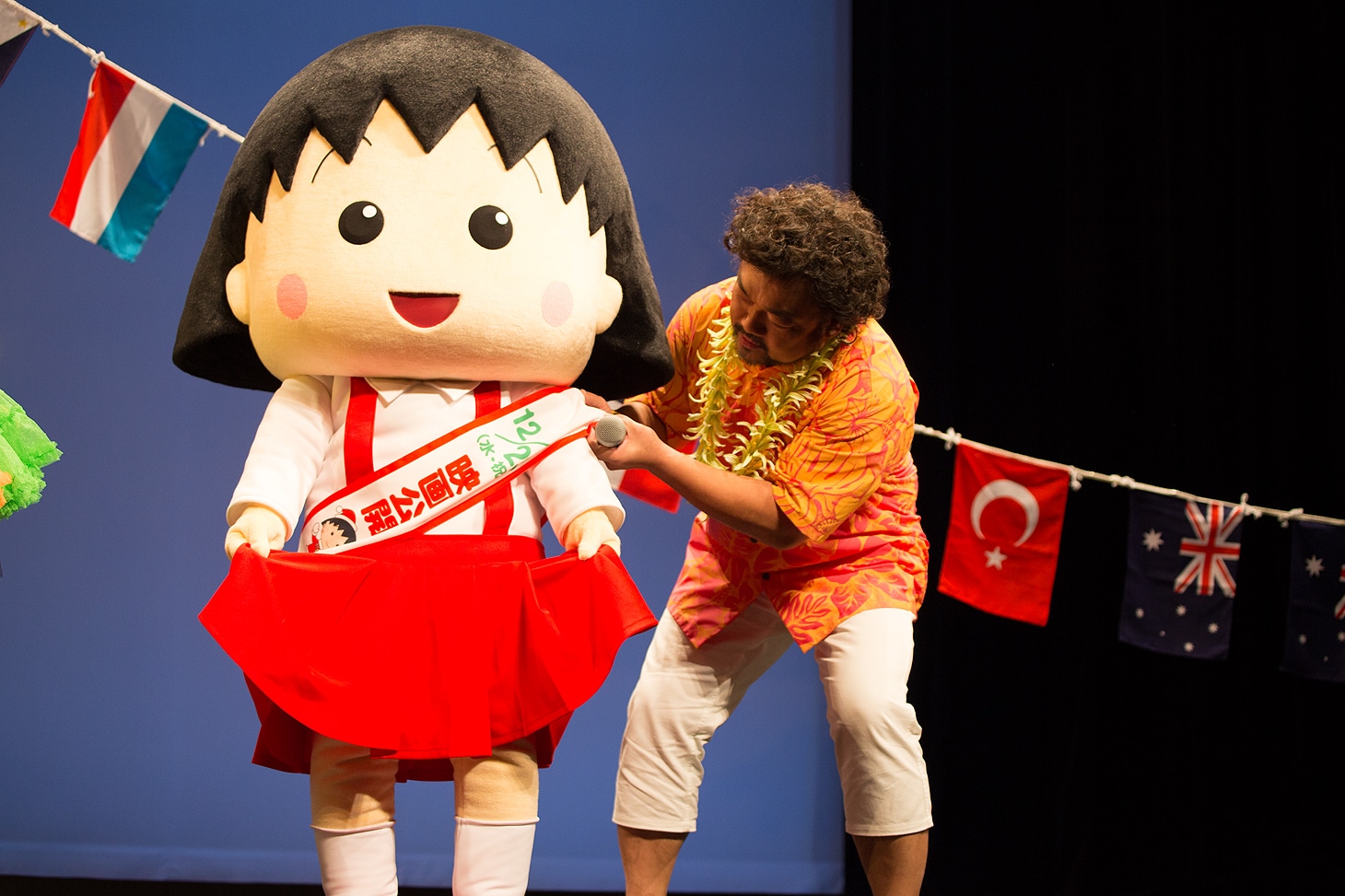 まる子（左）のずれたたすきを直してあげるパパイヤ鈴木（右）。
