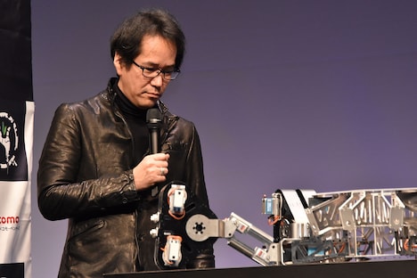 1/2サイズのタチコマのプロトタイプに興味津々な様子をみせる神山健治。