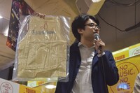 新井浩文が実際に着用したエプロンを取り出し「真空パックにするのに2500円かかりました。お金使うところを間違えました」と話す岡下慶仁ディレクター。