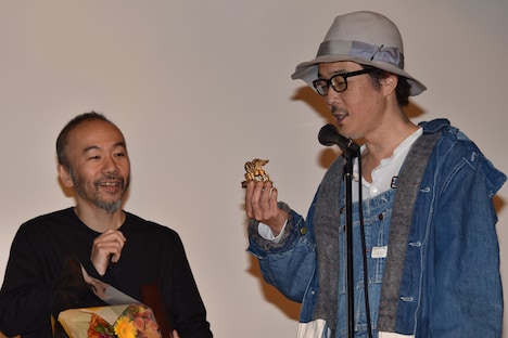 金獅子のトロフィーの説明をするリリー・フランキー（右）と、笑みを見せる塚本晋也（左）。
