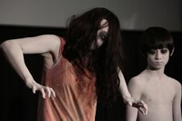 カメラ目線の伽椰子（左）と、それを冷めた目で見つめる俊雄（右）。