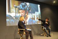 ヘッドセット型カメラを装着する岡田将生のメイキング写真を見ながら解説する大友啓史（右）。