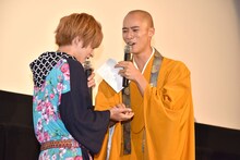 西銘駿（左）に御成フィギュアを手渡す柳喬之（右）。