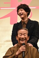小松政夫（前）の肩を揉む坂口健太郎（後）。