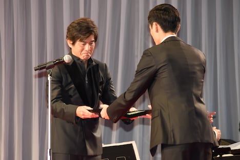 高良健吾(手前)から楯を受け取った佐藤浩市(奥)。