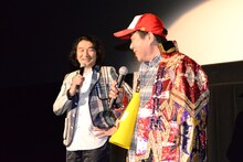 新日本プロレス所属オカダ・カズチカのガウンを羽織っている木村ひさし（右）と、その格好にツッコミを入れる池田鉄洋（左）。