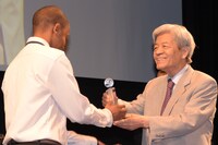 「水を、ください」の監督ムルー・ゴドラ（左）にトロフィーを渡す田原総一朗（右）。