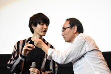 桜田通（左）に抽選で引いた席番号を読んでもらう金田治（右）。