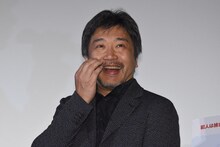 一言挨拶の前に椅子に腰掛けてしまい、照れ笑いを浮かべた是枝裕和。