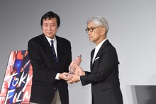 フェスティバルディレクターの久松猛朗（左）から、トロフィーを受け取る坂本龍一（右）。