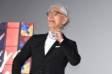 トロフィーをナイフのように首に当てておどける坂本龍一。