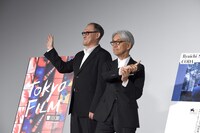 ムービーカメラに向かって手を振るスティーブン・ノムラ・シブル（左）と、坂本龍一（右）。