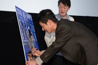 「映画監督 原恵一の世界」のメインビジュアルにサインをする加瀬亮。