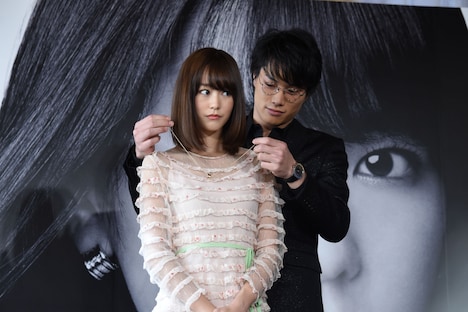 桐谷美玲（手前）にブルガリのネックレスを着ける鈴木伸之（奥）。