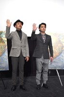 ムービーカメラに向かってゆっくりと手を振る山田孝之（右）とFROGMAN（左）。