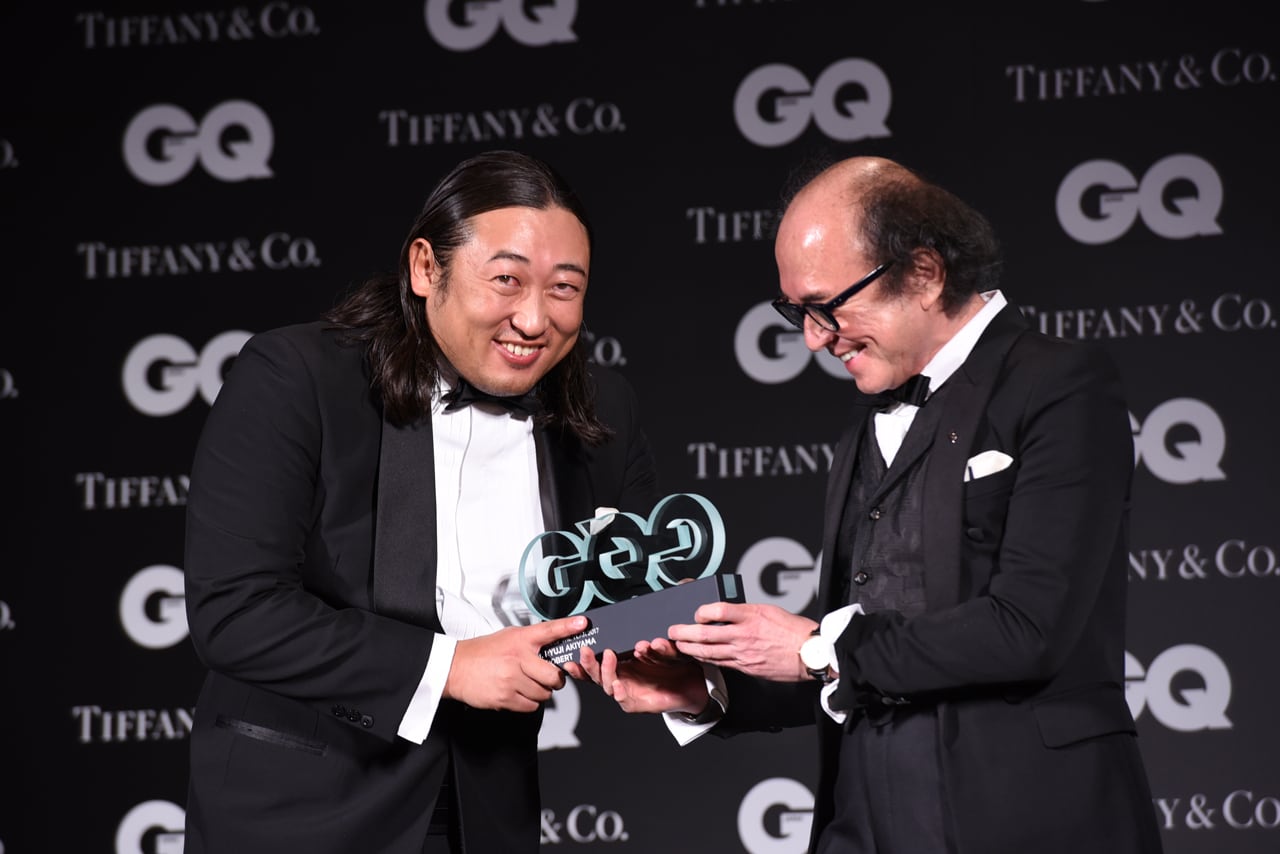 「GQ JAPAN」の鈴木正文編集長（右）からトロフィーを受け取るロバート秋山（左）。